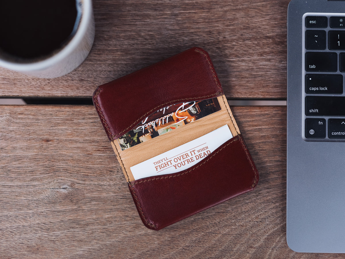 Slim Business Card Holder in Oxblood with cards inside, on a wooden desk beside a laptop and coffee