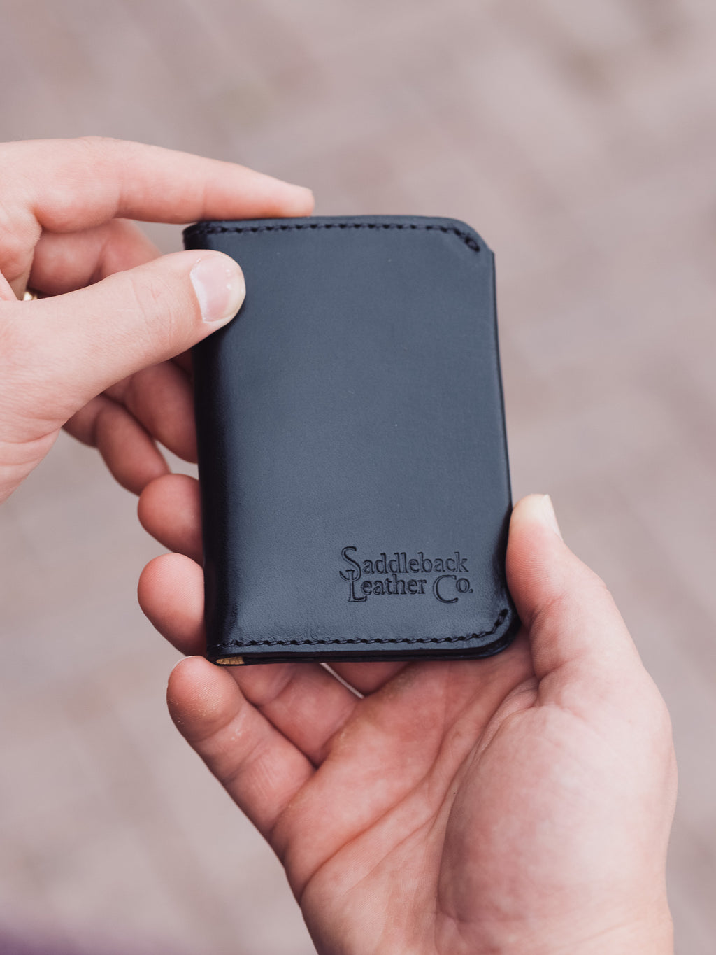 Slim Bifold Wallet in Black, held closed in hand showing the embossed logo