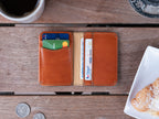 Slim Bifold Wallet in English Tan, open with cards on a wooden table beside coffee and a pastry