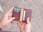 Slim Bifold Wallet in Oxblood, held open in hands showing cards in the slots