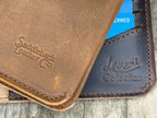 New Big Wallet in Tobacco, close-up of embossed logo resting on a dark brown wallet with embossed collection mark