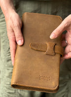 New Big Wallet in Tobacco held closed in both hands showing strap closure and embossed logo