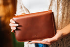 Magnetic Fold Over Bag Medium in Chestnut, held in both hands showing the embossed Love 41 logo on the flap