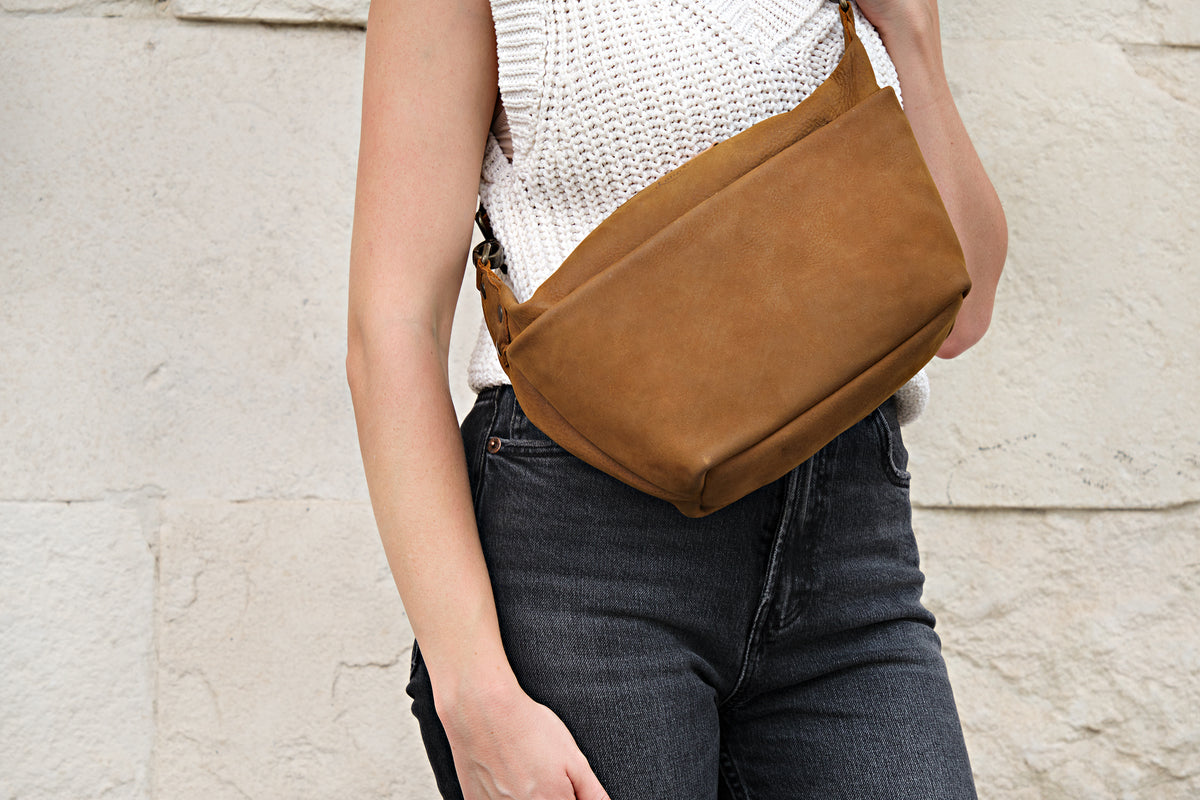London Sling Small in Tobacco, close-up worn at the waist over dark jeans against a stone wall