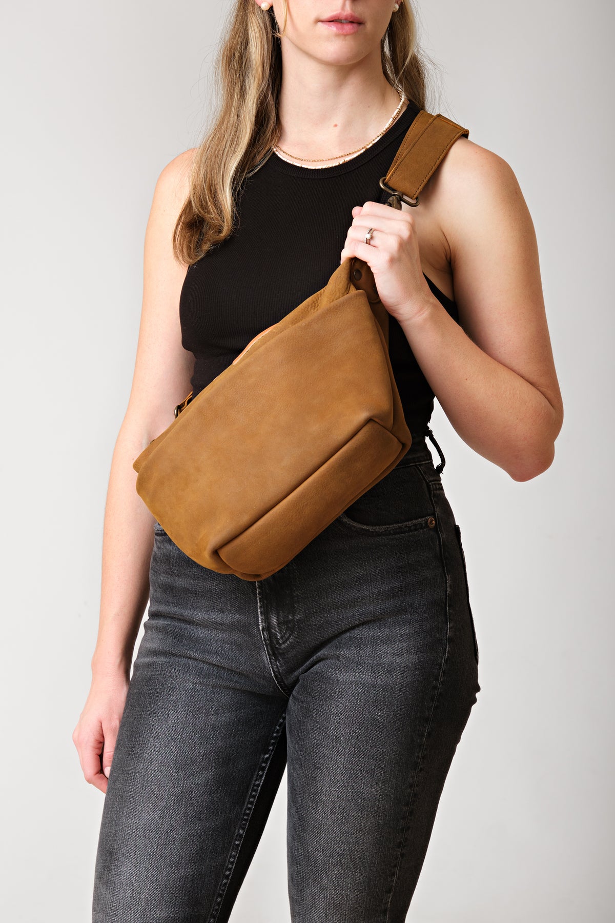 London Sling Large in Tobacco, worn across the chest by a woman in a black tank top and jeans