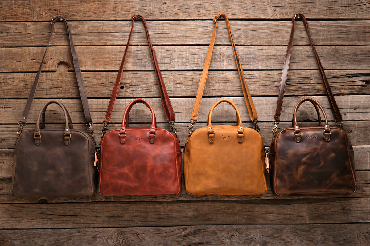 Professional Leather Satchel in Black, Chestnut, Tobacco and Dark Coffee Brown hanging side by side on a wood wall