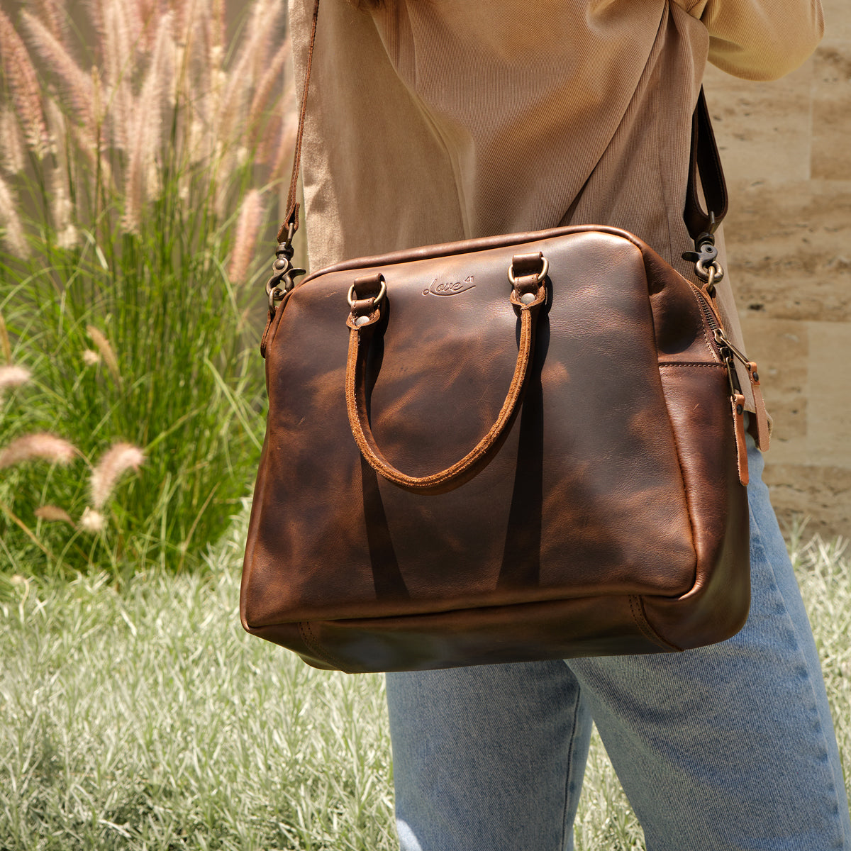 Professional Leather Satchel in Dark Coffee Brown, worn on the shoulder outdoors beside tall ornamental grass