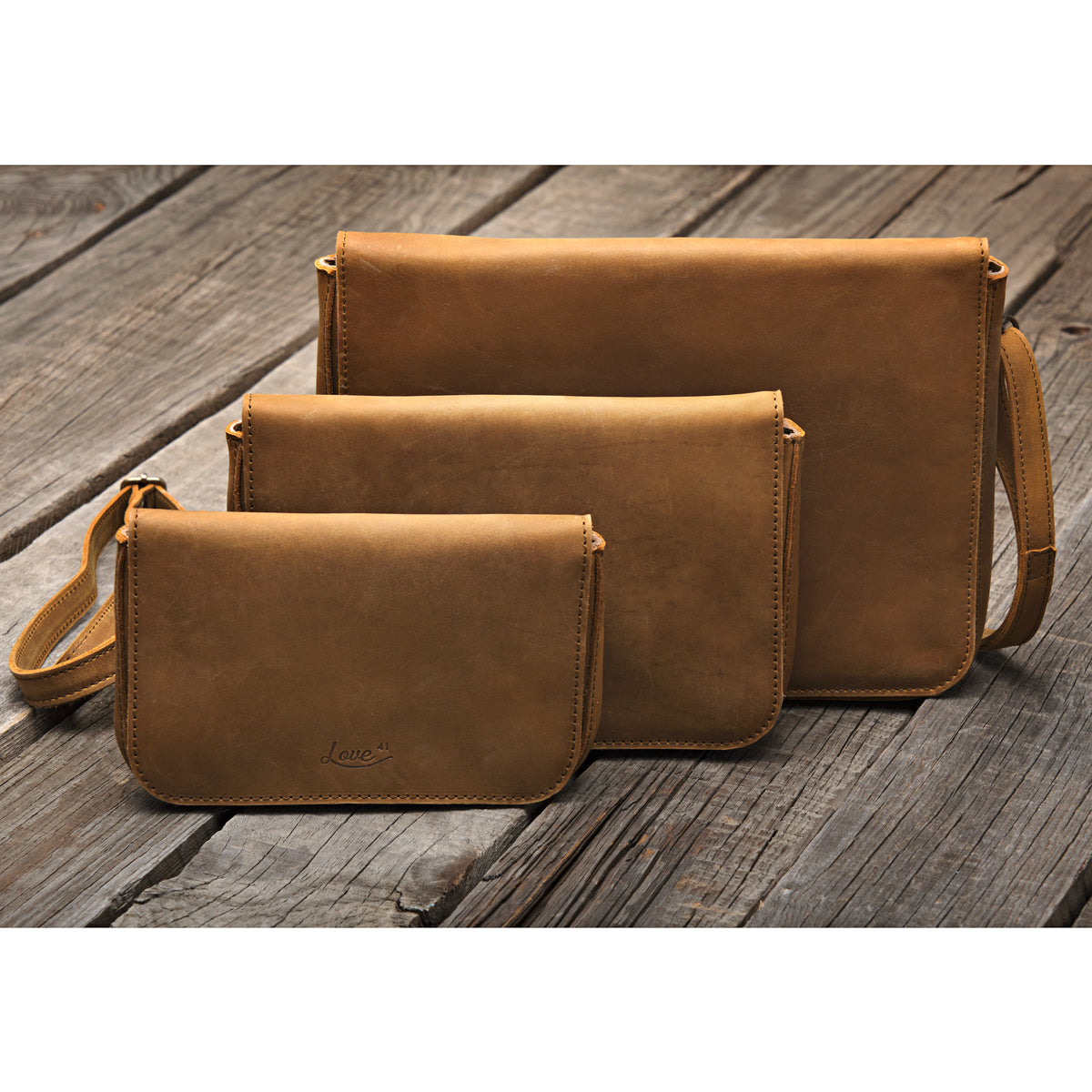Magnetic Fold Over Bag in Tobacco, three sizes lined up from small to large on weathered wood planks