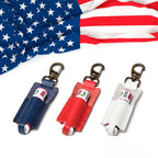 Leather lip balm holder keychains in navy blue, red and white with brass clips beneath an American flag