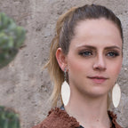 Leather Feather Earrings in White worn by a woman with her hair in a ponytail against a stone wall