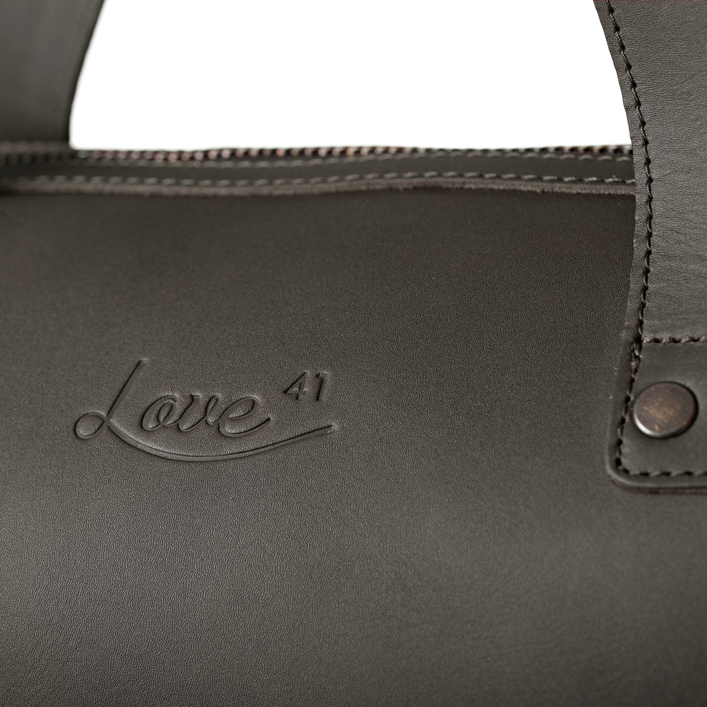 Simple Overnight Leather Duffle Bag in Black, close-up of the embossed Love 41 logo and riveted handle