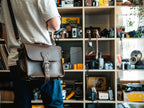 Photographer's Satchel in Dark Coffee Brown, carried by a man in front of shelves of vintage cameras
