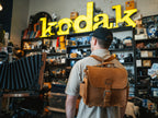 Photographer's Satchel in Tobacco, worn as a backpack by a man inside a vintage camera shop