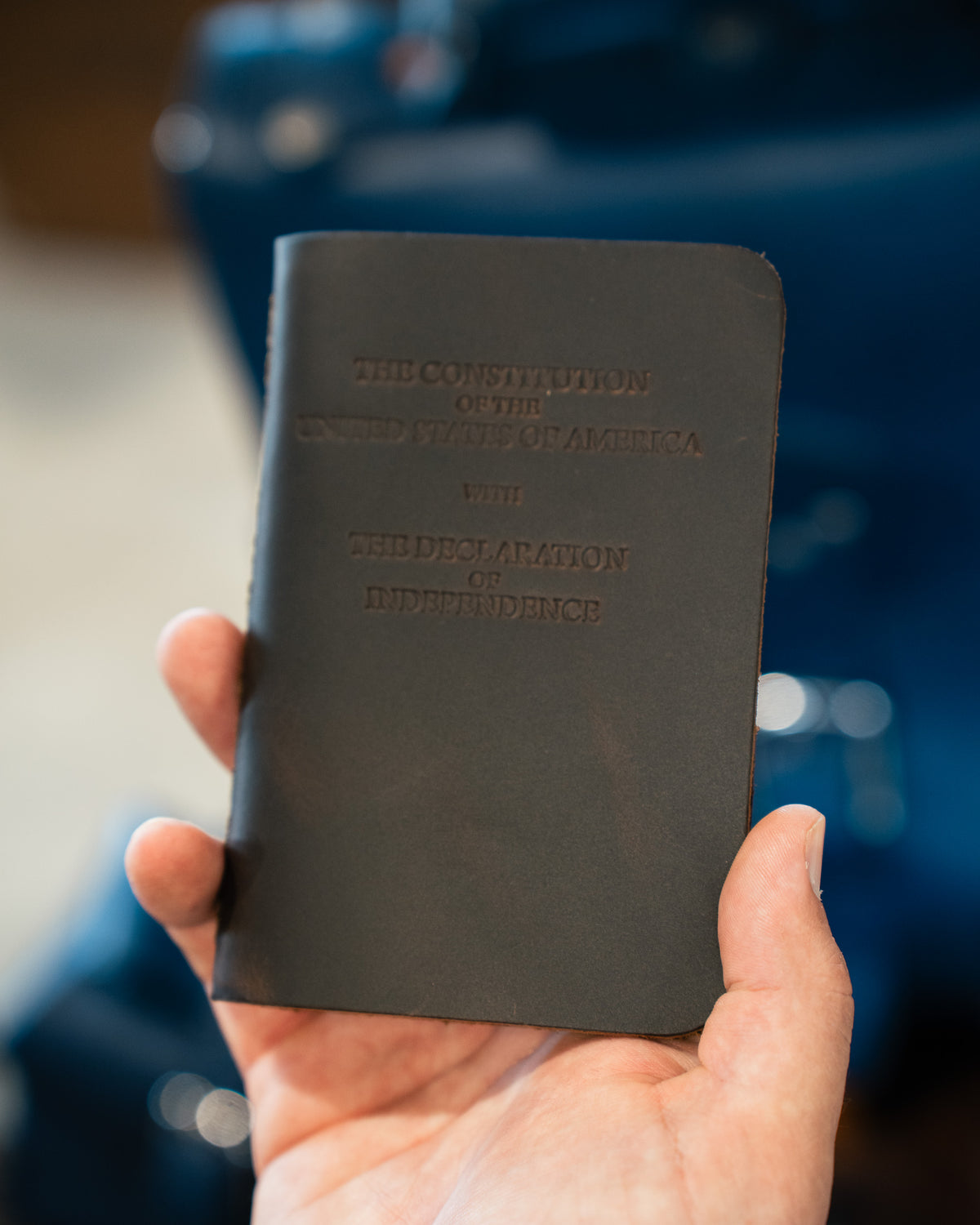Pocket Declaration/Constitution in black leather held in one hand, embossed title on the cover