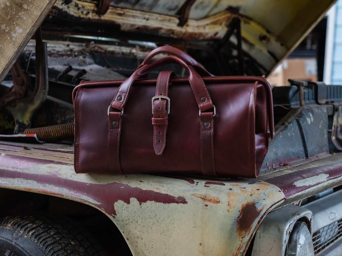Leather Range and Tool Bag in Chestnut on the rusty fender of an old truck with its hood open
