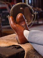 Wingtip Shoes in Natural Tan, crossed feet on a sheepskin in front of a round mirror