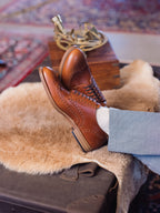 Wingtip Shoes in Natural Tan, crossed feet resting on a sheepskin over a vintage trunk