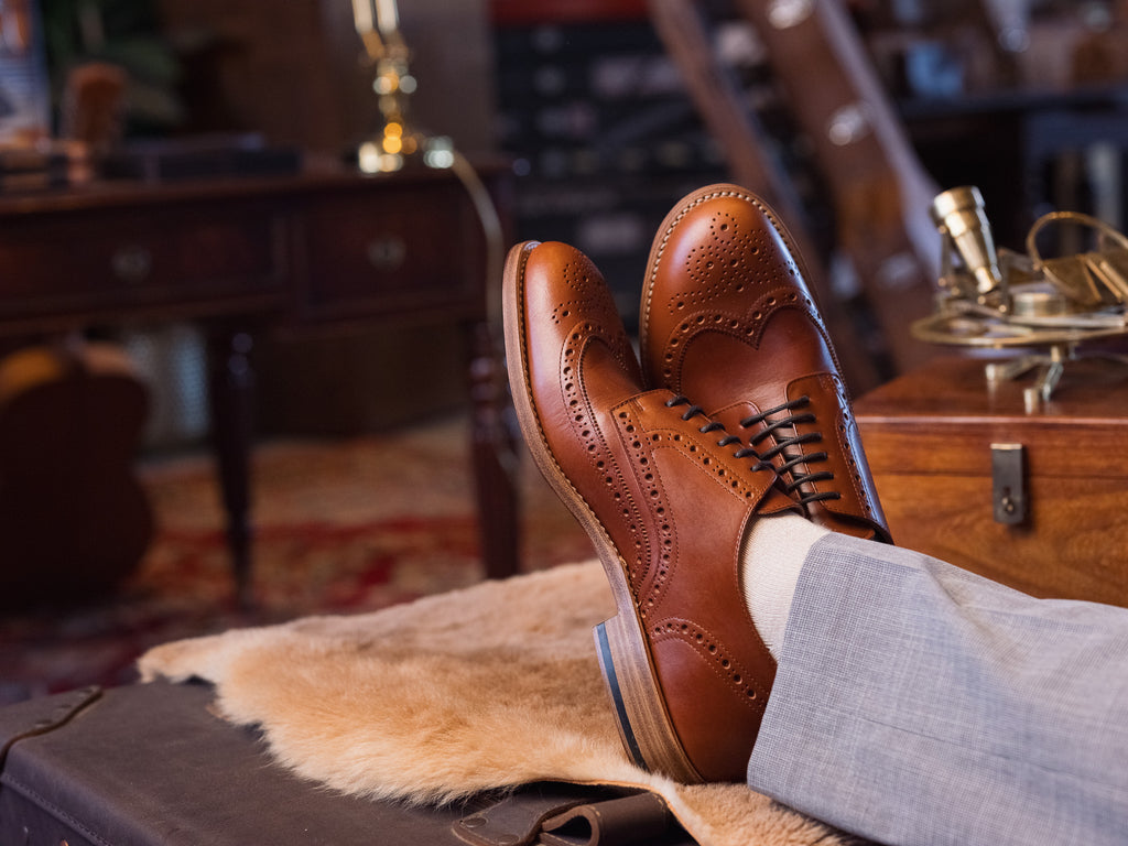 Wingtip Shoes in Natural Tan, crossed feet propped on a sheepskin in a vintage study