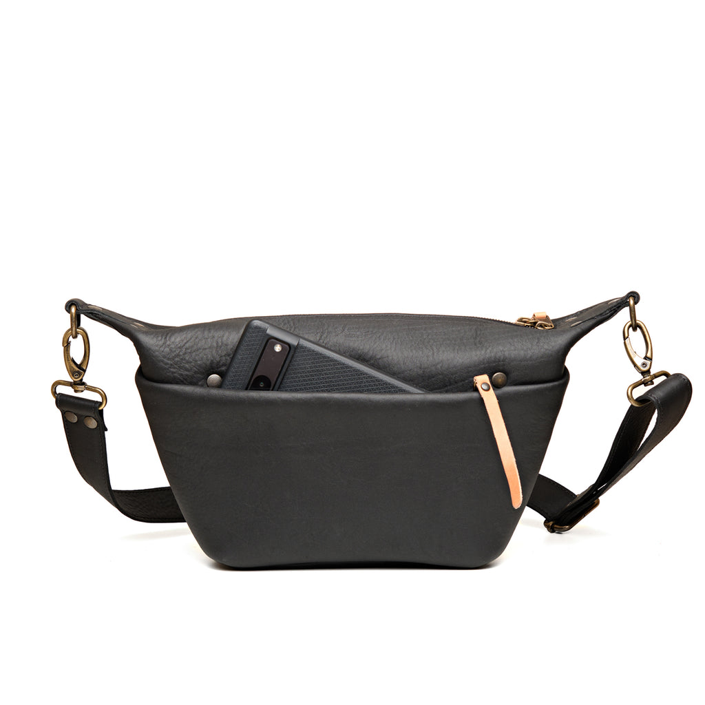 London Sling Small in Black, front view with a phone tucked in the snap pocket