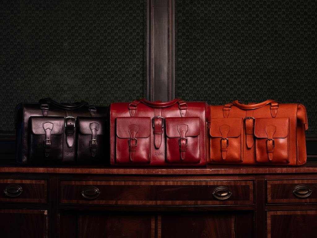 Blackstone Barrister Briefcase in Raven Black, Oxblood and English Tan lined up on a wooden sideboard