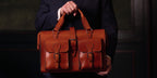 Blackstone Barrister Briefcase in English Tan held by its handles in front of a man in a dark suit