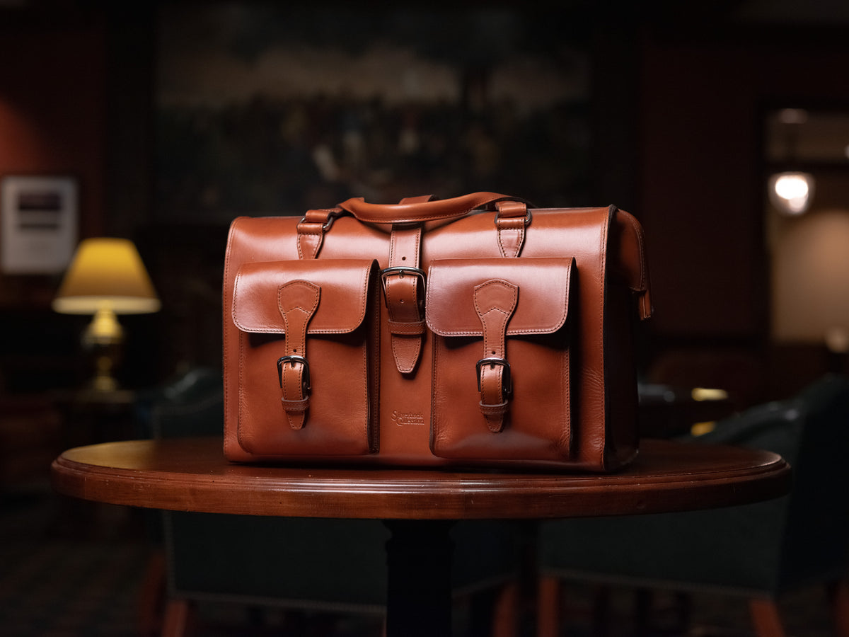 Blackstone Barrister Briefcase in English Tan on a round wooden table in a dim lamp-lit lounge
