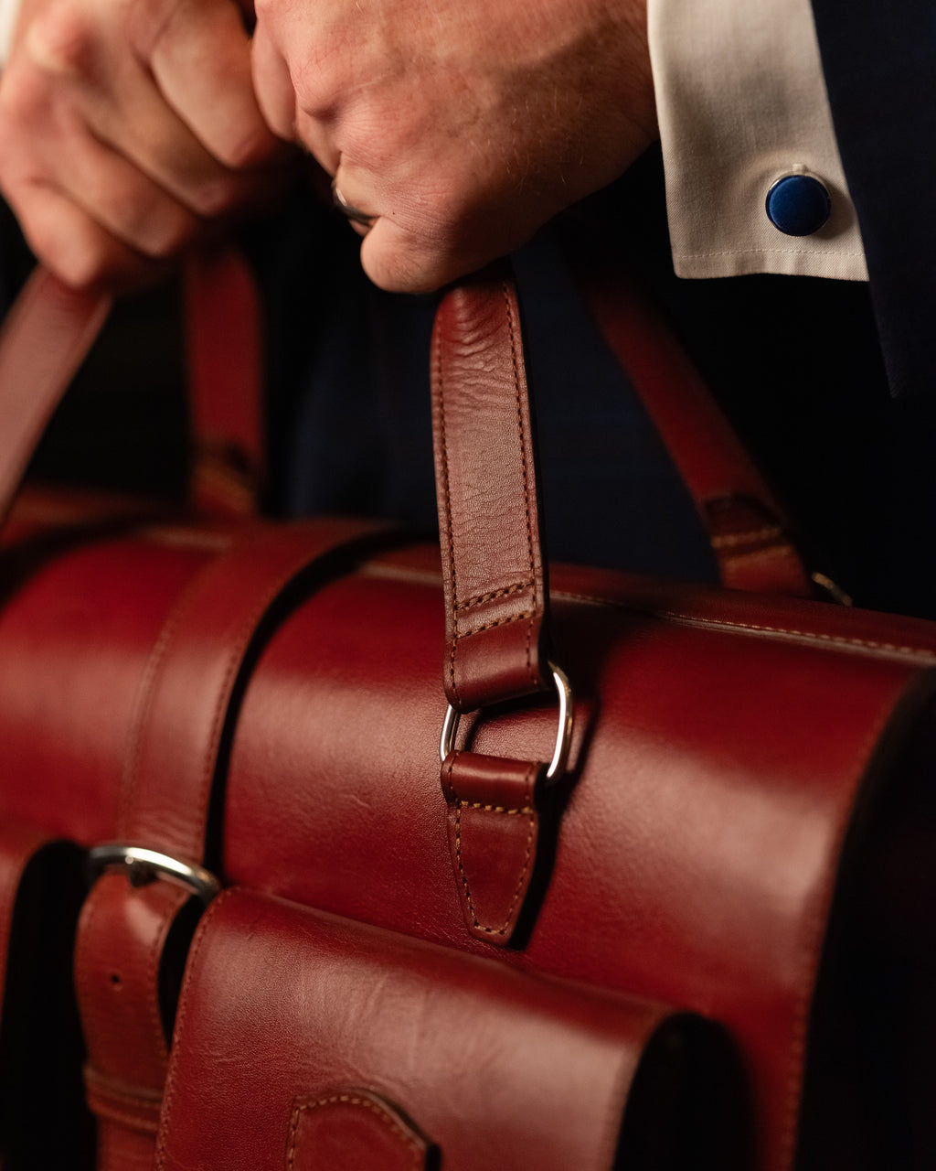 Blackstone Barrister Briefcase in Oxblood, close-up of the handle strap, metal ring and stitching held in hand