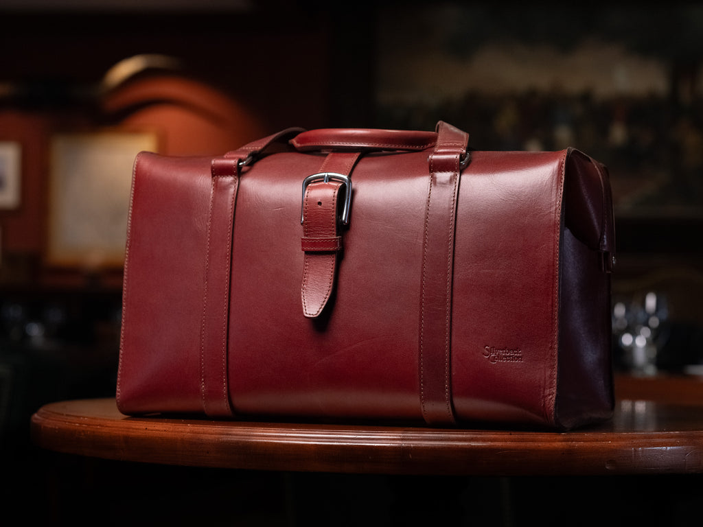 Taylor Duffle Bag in Oxblood on a round wooden table in a dimly lit room