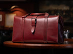 Taylor Duffle Bag in Oxblood on a round wooden table in a dimly lit room