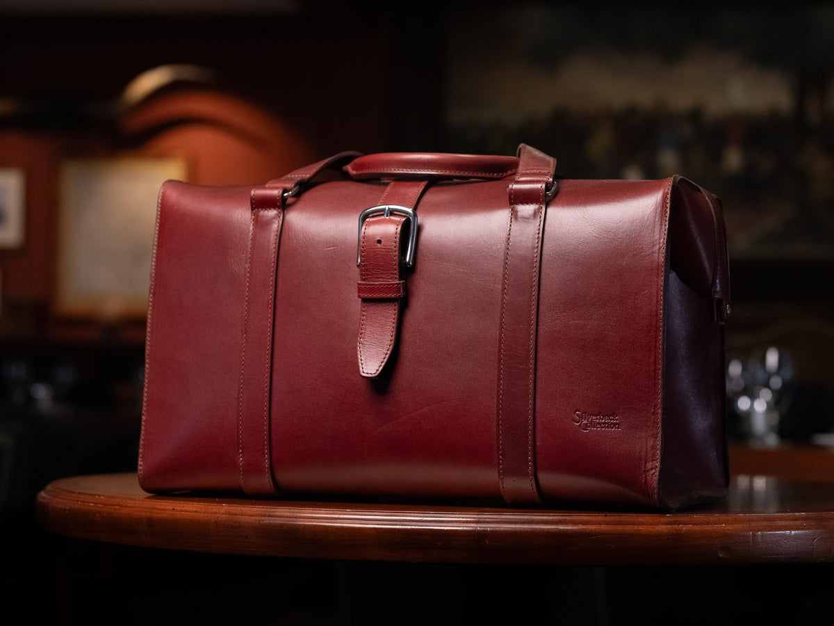 Taylor Duffle Bag in Oxblood on a round wooden table in a dimly lit room