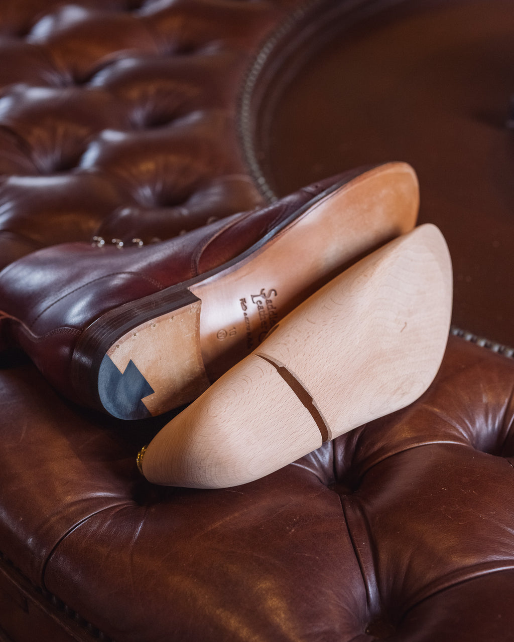Shoe Tree laid against the leather sole of a brown boot on a tufted leather ottoman