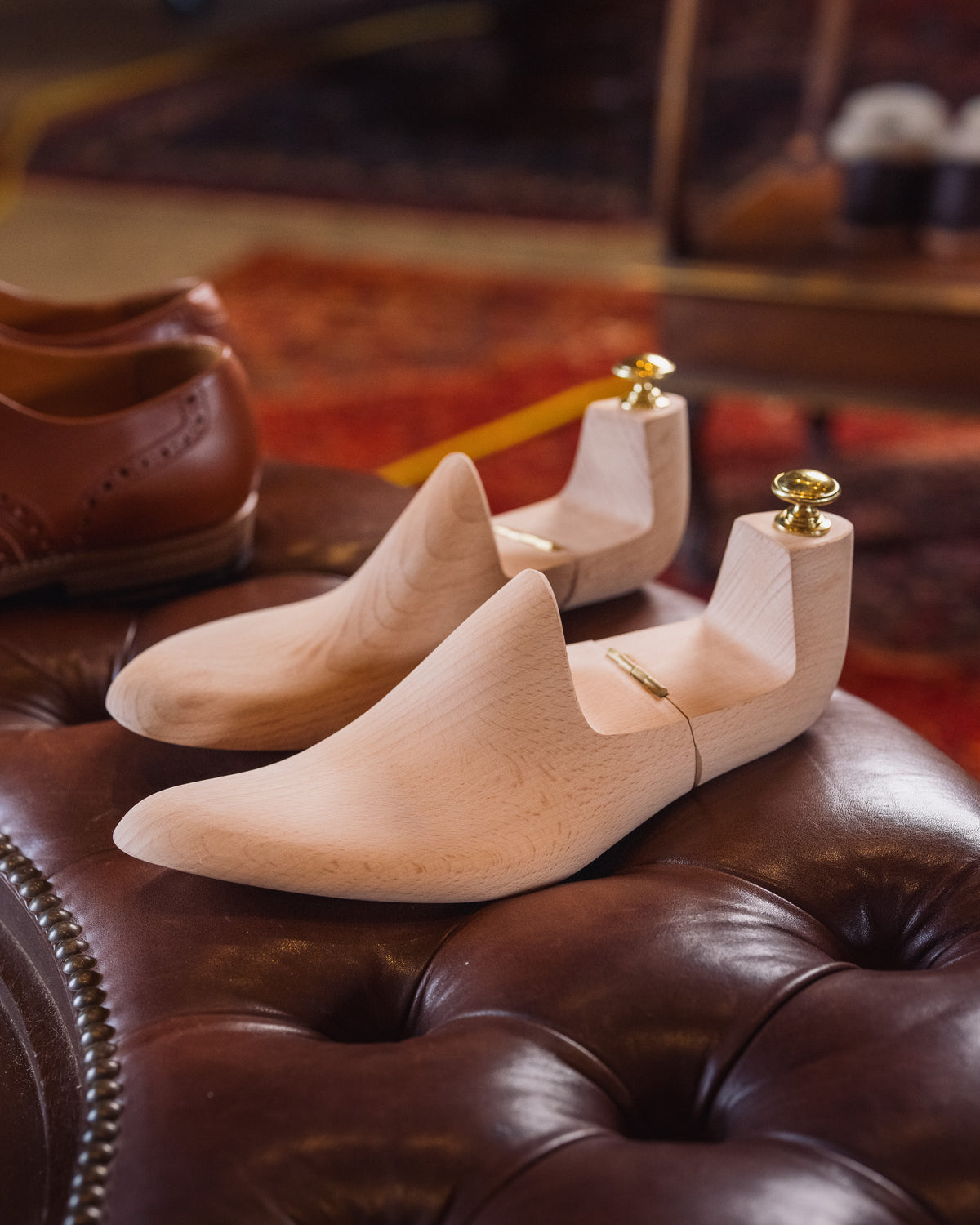 Shoe Tree pair in natural wood with brass knobs on a tufted leather ottoman