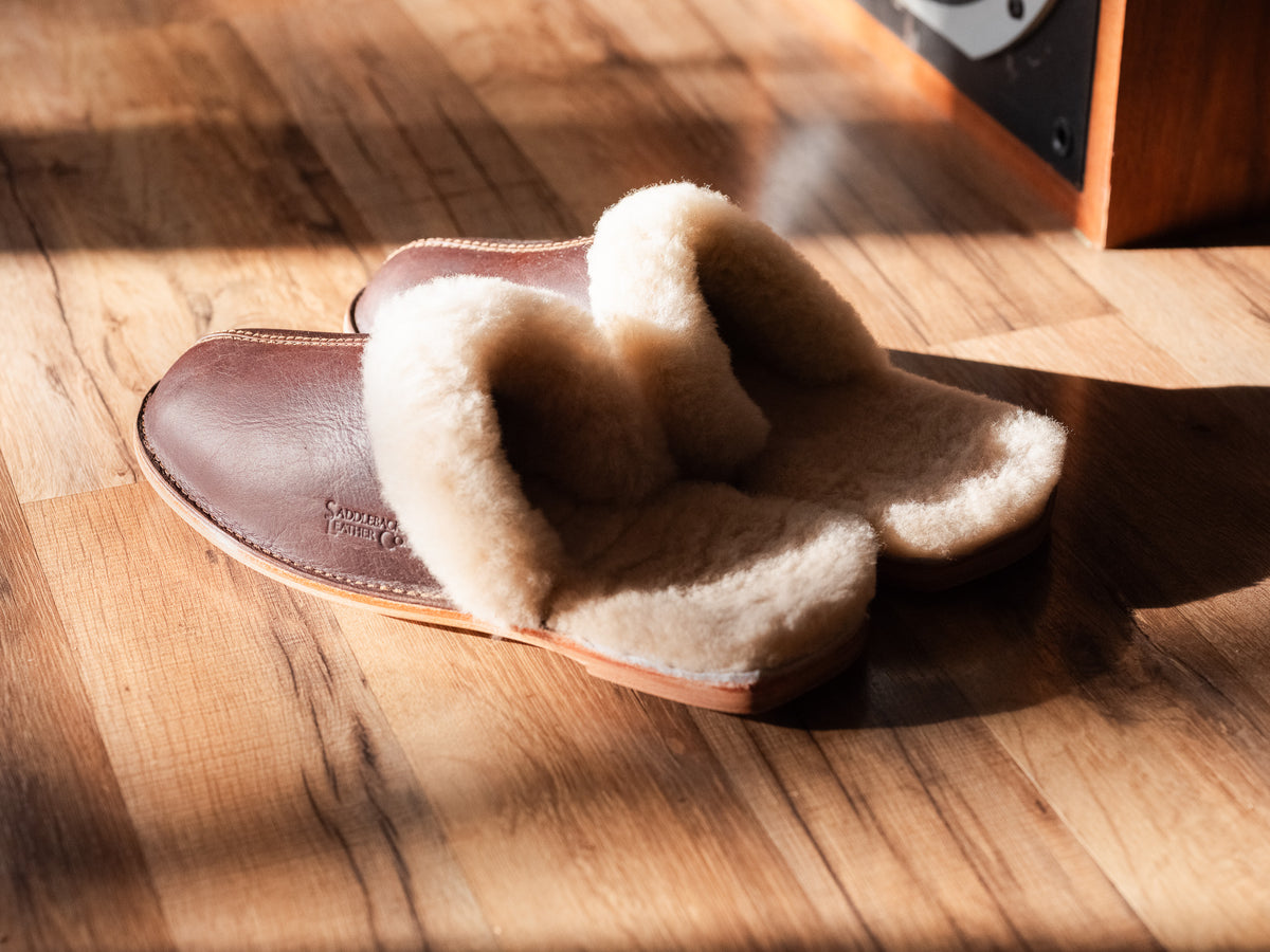 Men's Sheepskin Slippers in Dark Coffee Brown with thick sheepskin lining, in sunlight on a wood floor