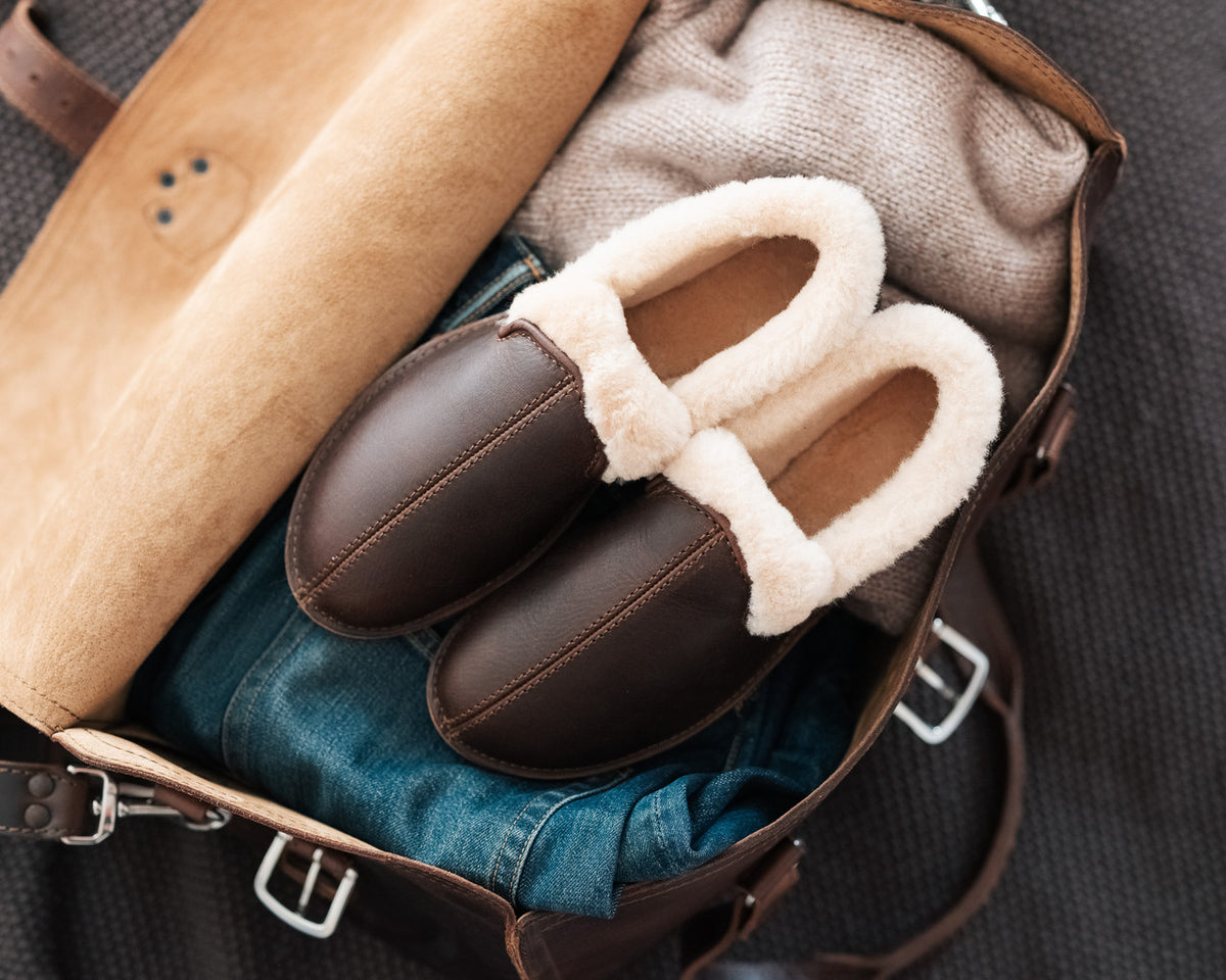 Pair of Sheepskin Moccasins in Dark Coffee Brown on jeans and a sweater in an open leather bag