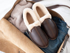 Pair of Sheepskin Moccasins in Dark Coffee Brown packed in an open leather bag with clothes, top view