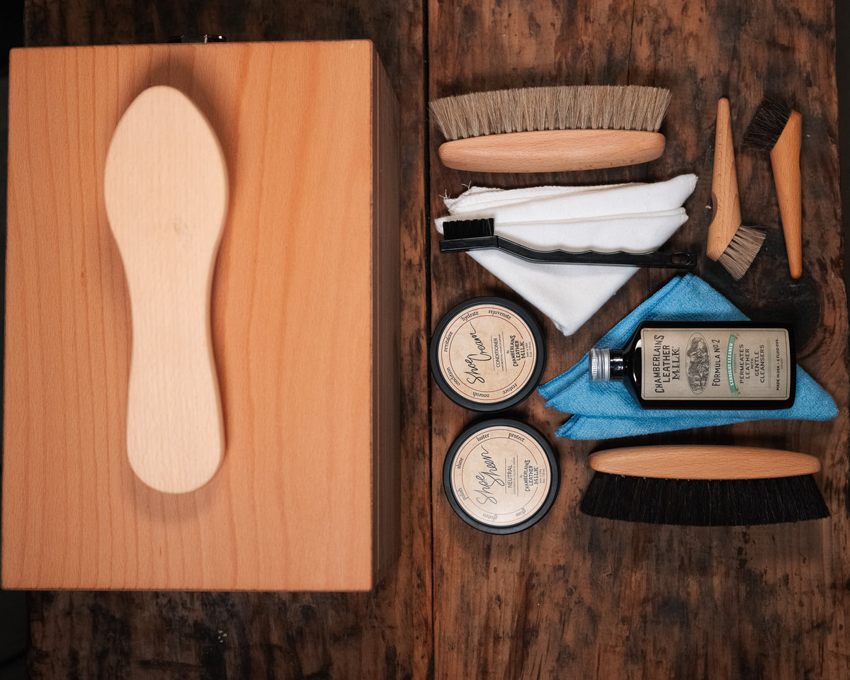 Luxury Shoe Shine Kit top view, wooden shine box with foot rest beside brushes, cream tins, leather care bottle and cloths