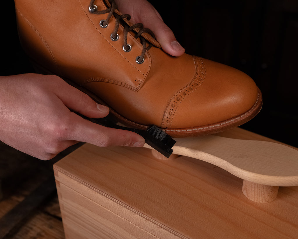 Luxury Shoe Shine Kit detail, hands using a welt brush along the sole of a tan leather boot on the shine stand