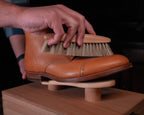 Luxury Shoe Shine Kit in use, a hand brushing a tan leather cap-toe boot on the wooden shine stand
