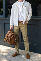 A man in a light jacket holding a tan leather bag, wearing Barefoot Slip-on Mules in Tobacco