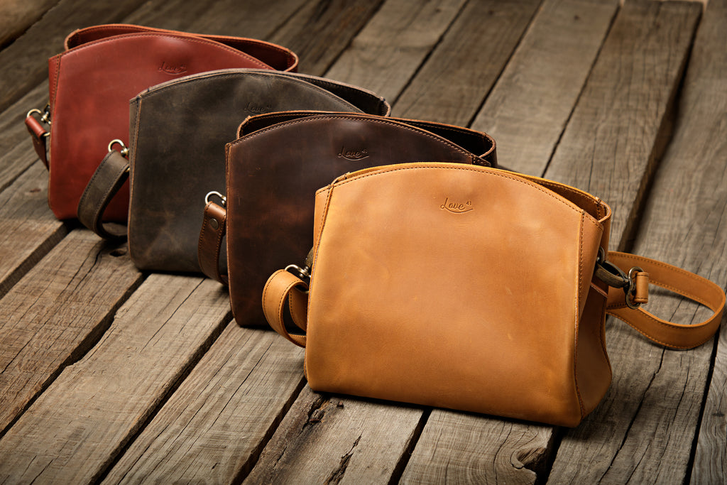 Leather Organizer Crossbody in Chestnut, Black, Dark Coffee Brown and Tobacco lined up on weathered wood planks