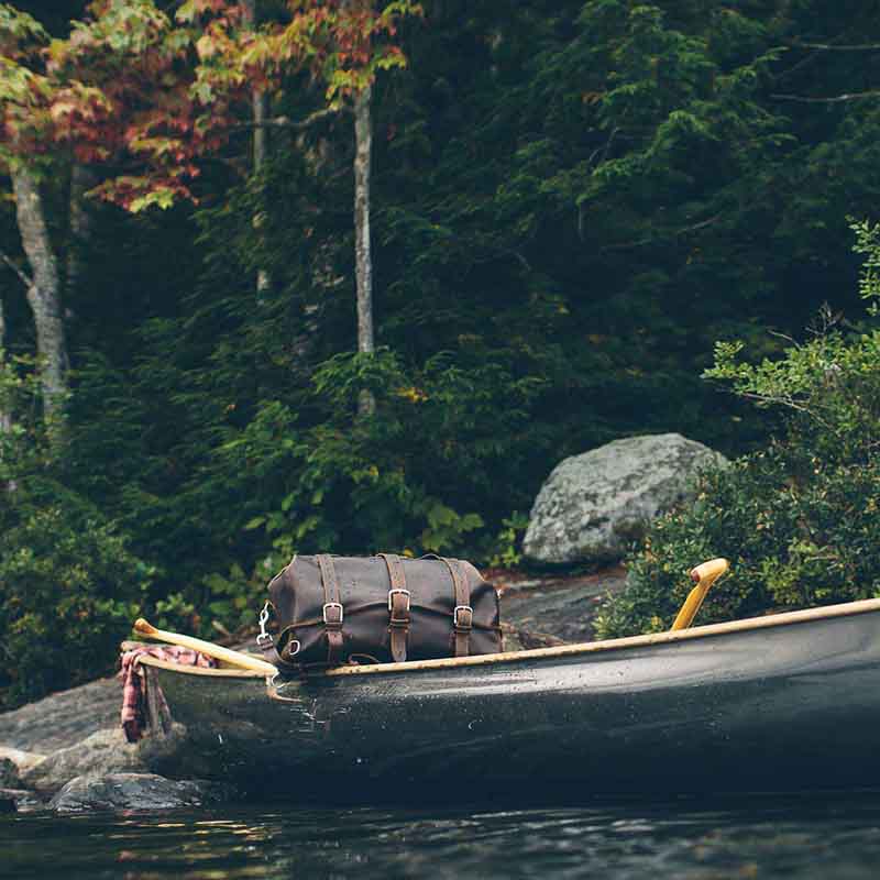 24" Waterbag in dark brown, resting in a canoe on a forest lake shore