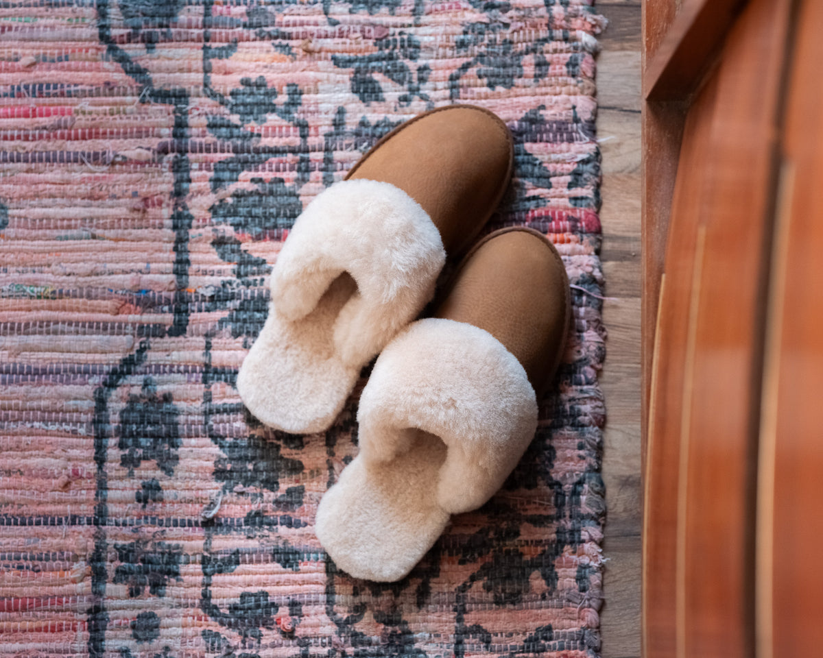 Women's Sheepskin Slippers in Tobacco, top-down view of pair on a patterned woven rug