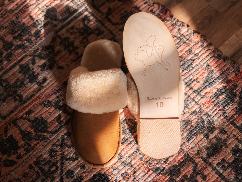 Women's Sheepskin Slippers in Tobacco, one slipper beside an upturned sole with stamped dog logo