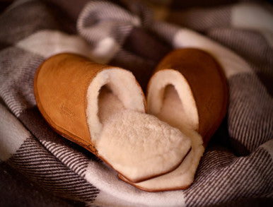Pair of Women's Sheepskin Slippers in Tobacco with shearling lining on a plaid blanket