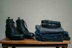 High quality black leather Officer Boots beside a black leather belt on folded jeans on a wooden table