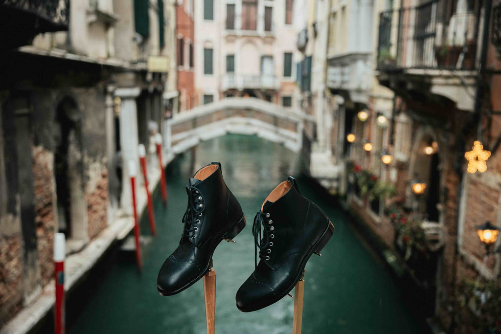 Officer's Boot in Raven Black, pair on wooden stands above a Venice canal