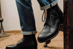 Officer's Boot in Raven Black, worn with cuffed jeans, one foot on a chair rung