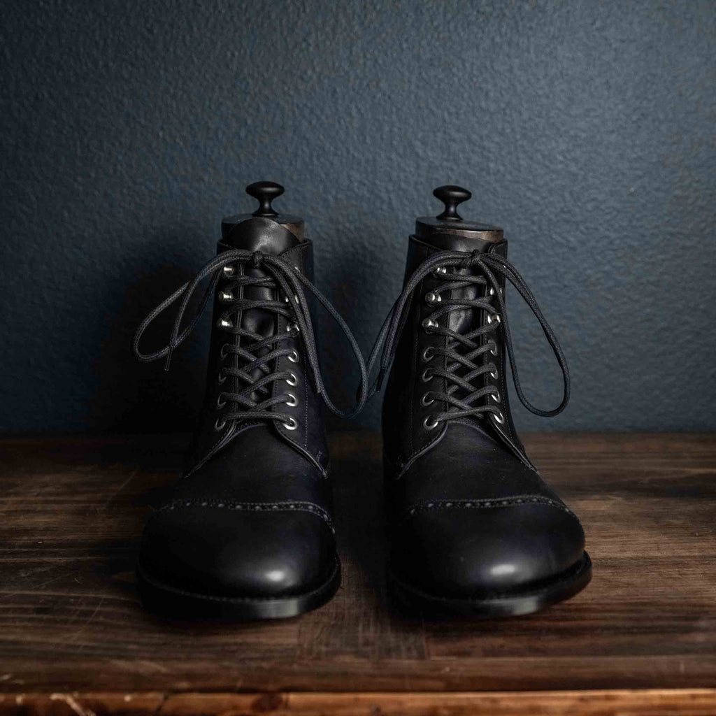 Officer's Boot in Raven Black, front view of the pair with shoe trees on a wooden table