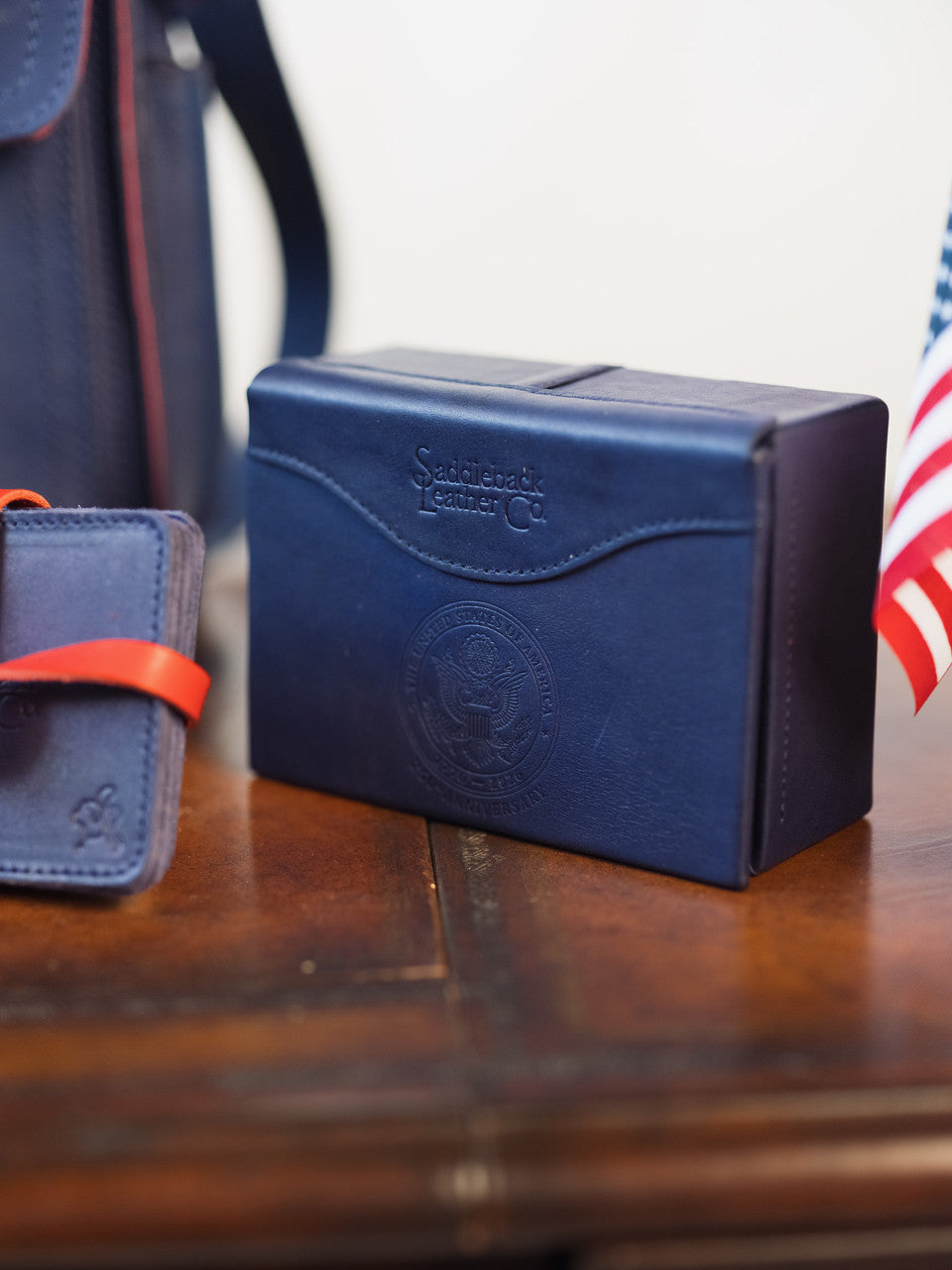 Saddleback Club Membership Thomas Jefferson Leather Desk Box in Blue and Red, closed on a wood desk with embossed seal