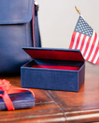 Saddleback Club Membership Thomas Jefferson Leather Desk Box in Blue and Red, open on a wood desk beside an American flag